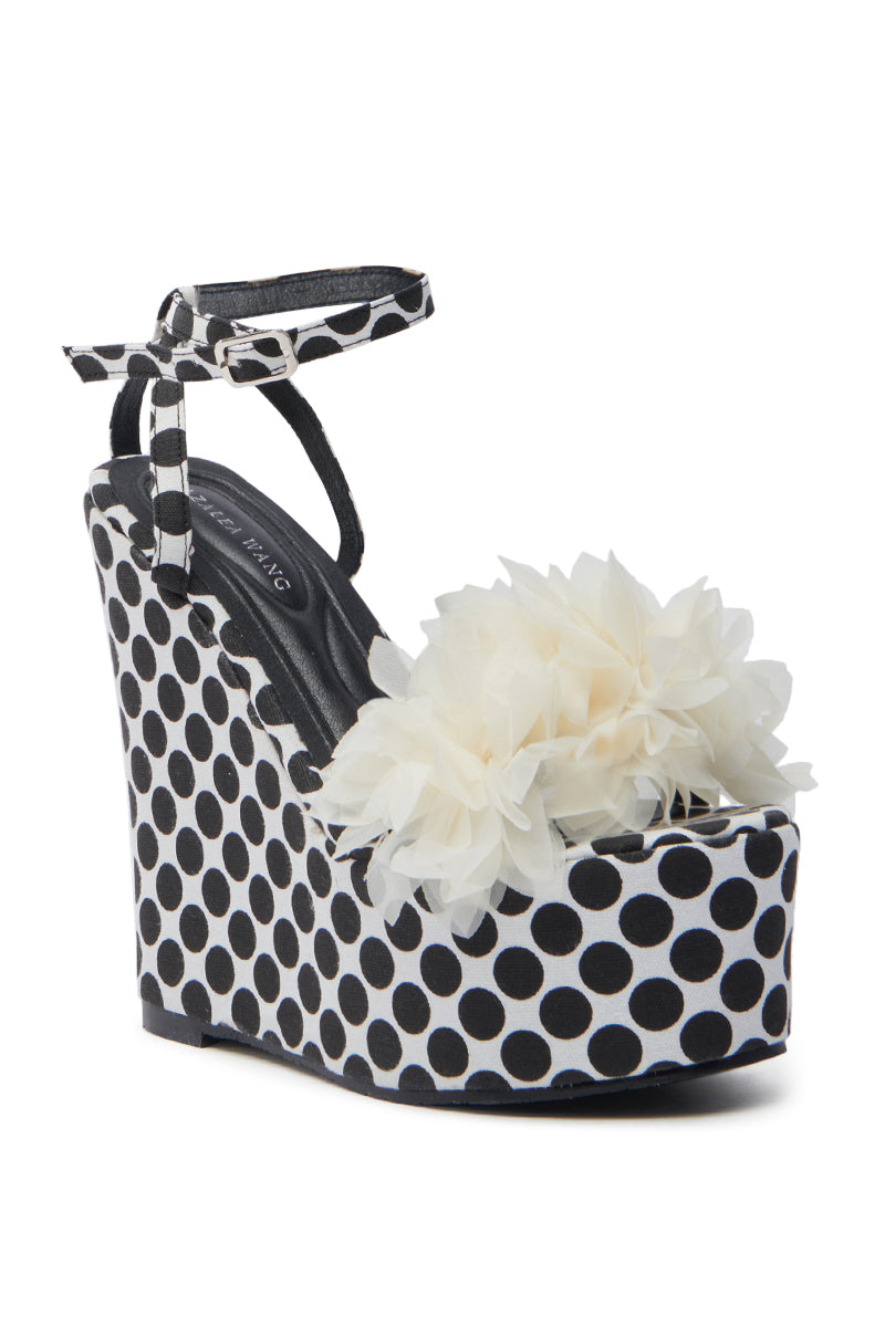 The AZALEA WANG SERAIAH BLACK AND WHITE POLKA DOT WEDGE SANDAL boasts a chic design with a secure ankle strap and buckle, enhanced by an off-white 3D tulle floral applique on the toe for playful elegance.