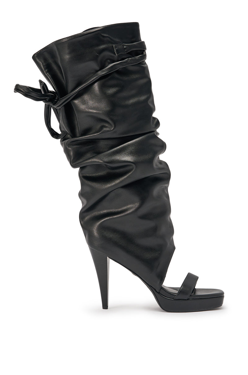 The AKIRA GOLD SEREL BLACK STILETTO GLADIATOR BOOT is a high-heeled, open-toe black boot with ruched design and a chic tie-up cuff, blending gladiator style with stiletto sandal elegance. 4