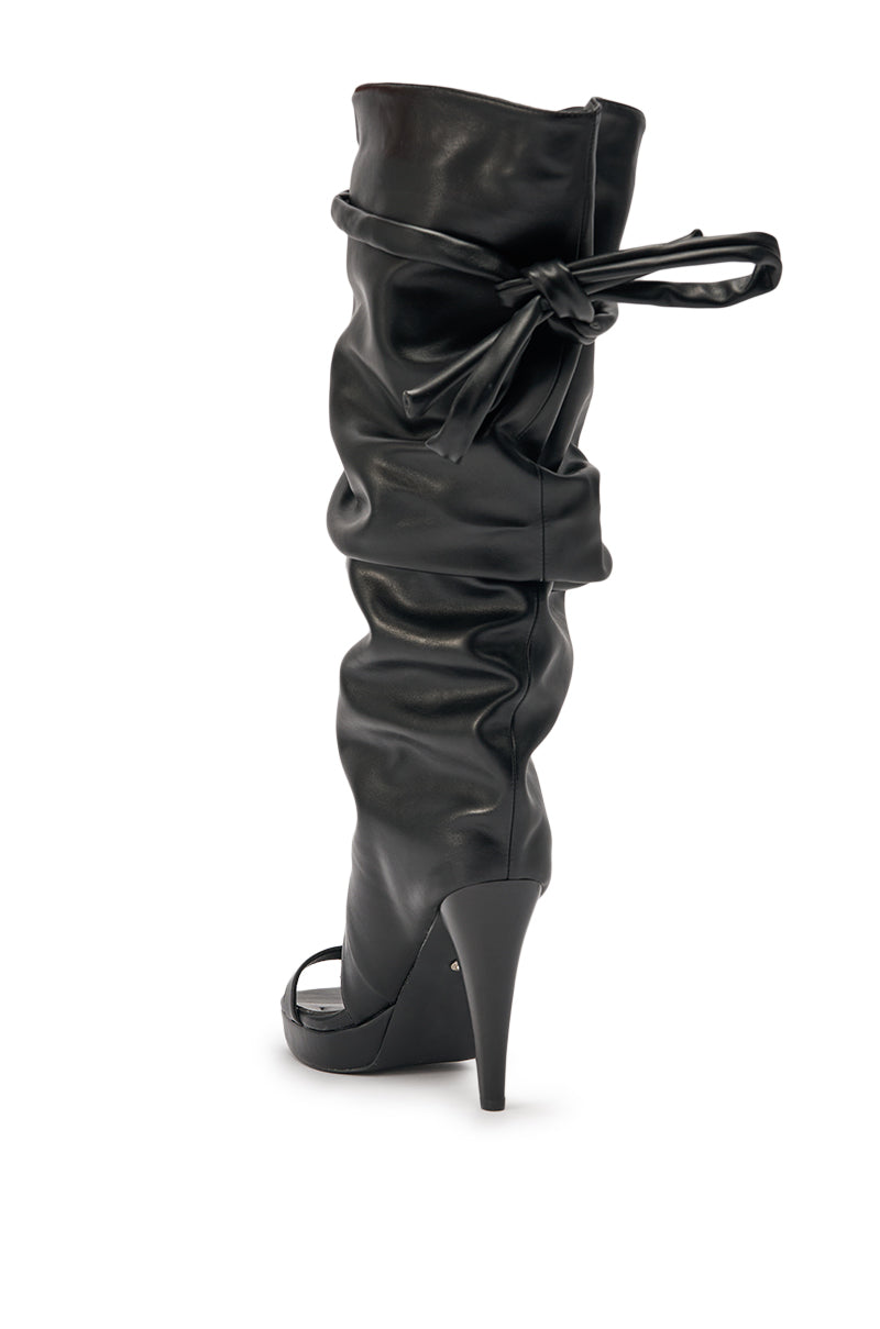 The AKIRA GOLD SEREL BLACK STILETTO GLADIATOR BOOT features a pointed toe, high stiletto heel, slouchy black leather, and a decorative tie-up cuff bow for added allure. 6
