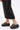 A person in black wide-leg pants stands on a white surface, wearing the AZALEA WANG SERGO BLACK EMBELLISHED CHUNKY SANDAL with a faux leather platform sole.