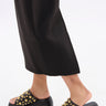 A person in black wide-leg pants stands on a white surface, wearing the AZALEA WANG SERGO BLACK EMBELLISHED CHUNKY SANDAL with a faux leather platform sole.
