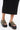 A person wearing a long black skirt and AZALEA WANG SERGO BLACK EMBELLISHED CHUNKY SANDALS stands on a white background.