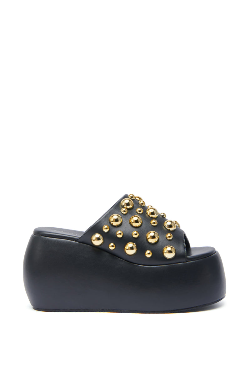 The AZALEA WANG SERGO BLACK EMBELLISHED CHUNKY SANDAL features a faux leather upper with multiple gold metallic studs, an open toe, and a thick platform sole.