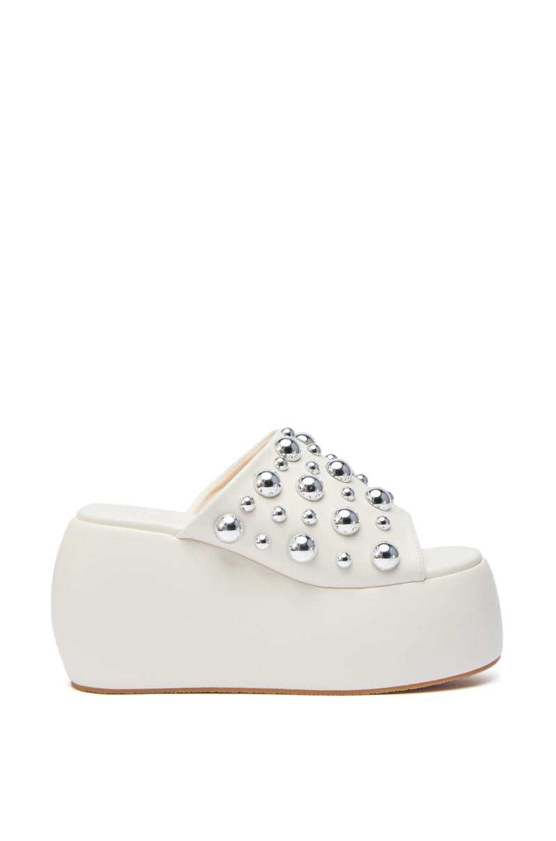 The AZALEA WANG SERGO BONE EMBELLISHED CHUNKY SANDAL is a white faux leather platform with an open toe, high wedge sole, and oversized metallic silver studs on the upper strap for a bold, embellished look.