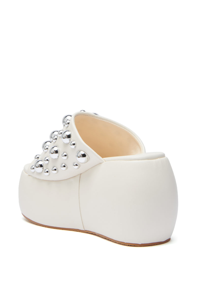 The AZALEA WANG SERGO BONE EMBELLISHED CHUNKY SANDAL is a white faux leather platform mule with a chunky heel, rounded toe, and metallic silver studs on the upper, displayed from an angled rear view on a white background.