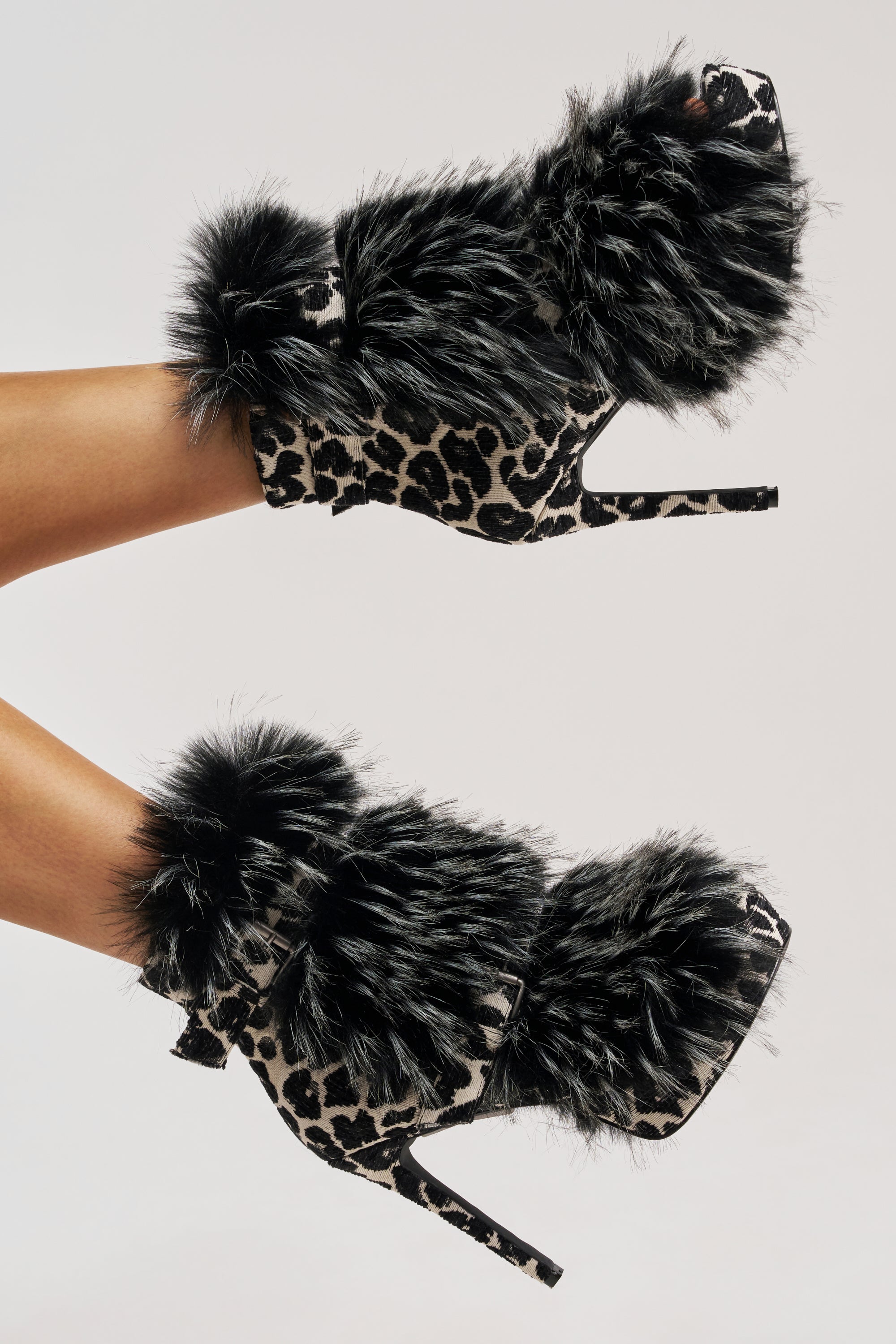 The AZALEA WANG SERIOUS Black and White Leopard with Fur Open Toe Stiletto Bootie features a platform sole, an animal print, and thick black faux fur trim, shown on raised legs against a plain background.