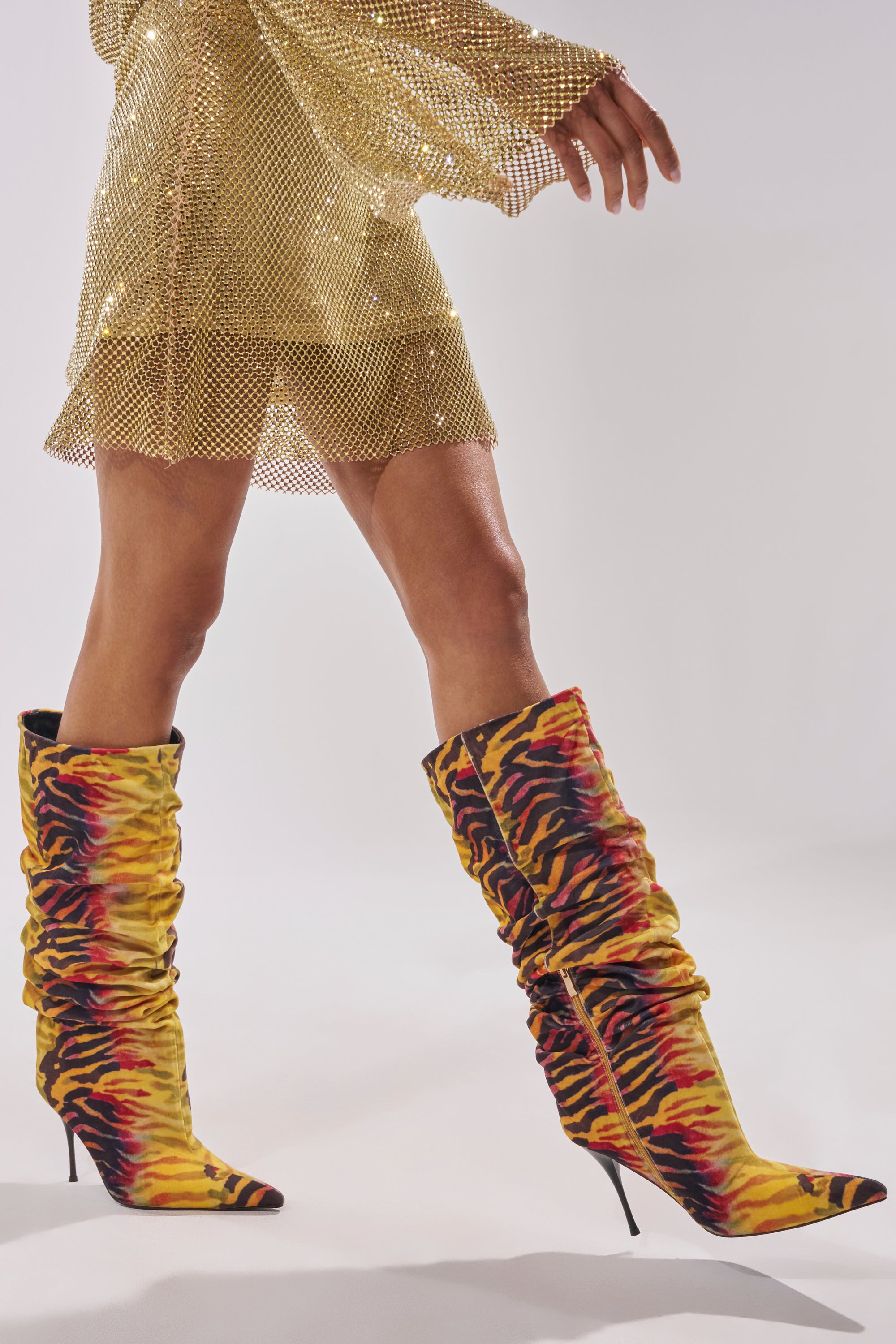A person wears a shimmering gold mesh dress and AZALEA WANG SERIOUSLY TIGER SLOUCHY STILETTO BOOTS, featuring a yellow tiger print and pointed heels in faux suede, against a light background. 0