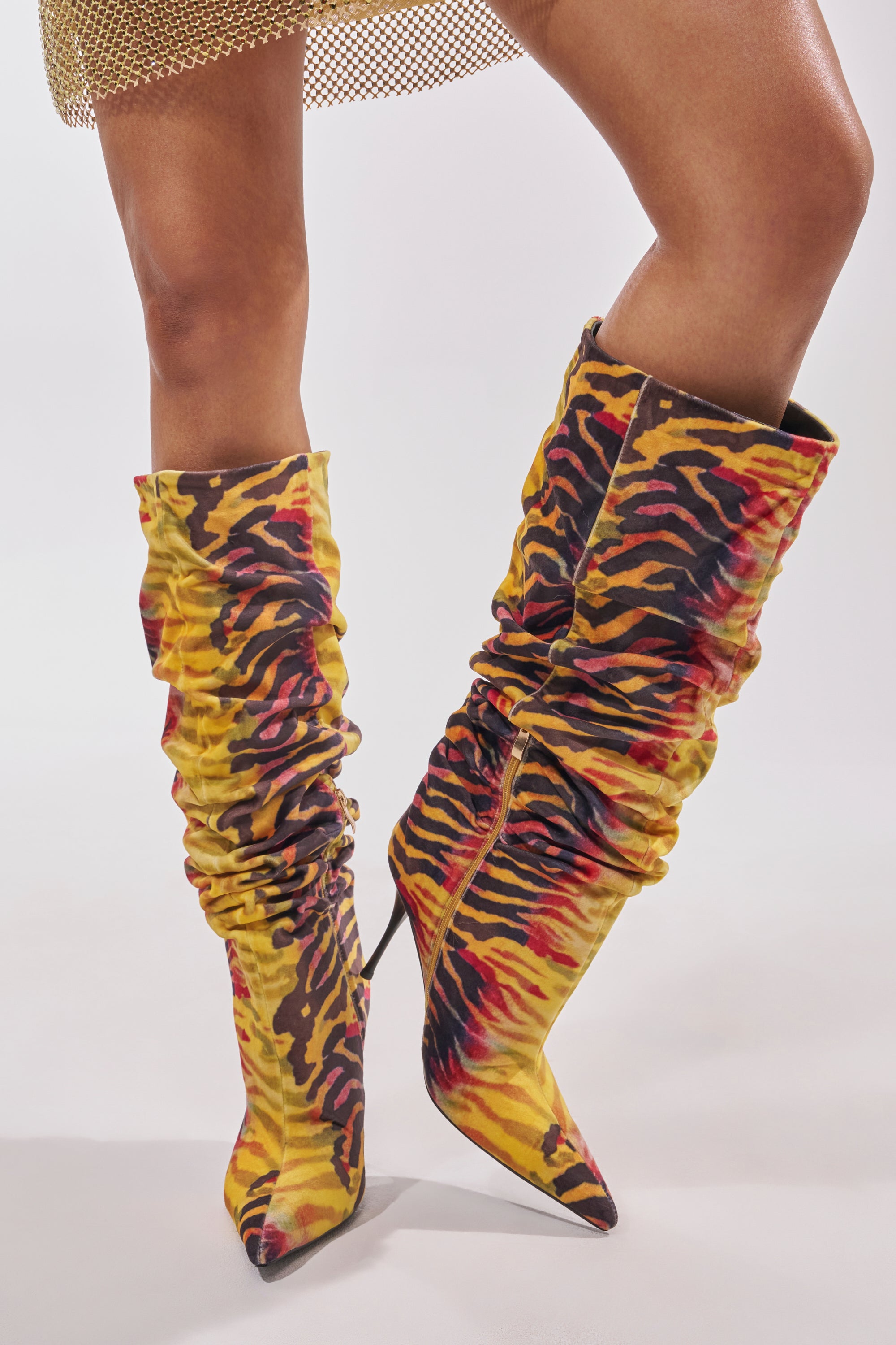 Wearing the AZALEA WANG SERIOUSLY TIGER SLOUCHY STILETTO BOOT—yellow tiger print faux suede knee-highs with pointed toes and a stiletto heel—styled with a gold mesh skirt for a bold, fierce fashion statement. 2