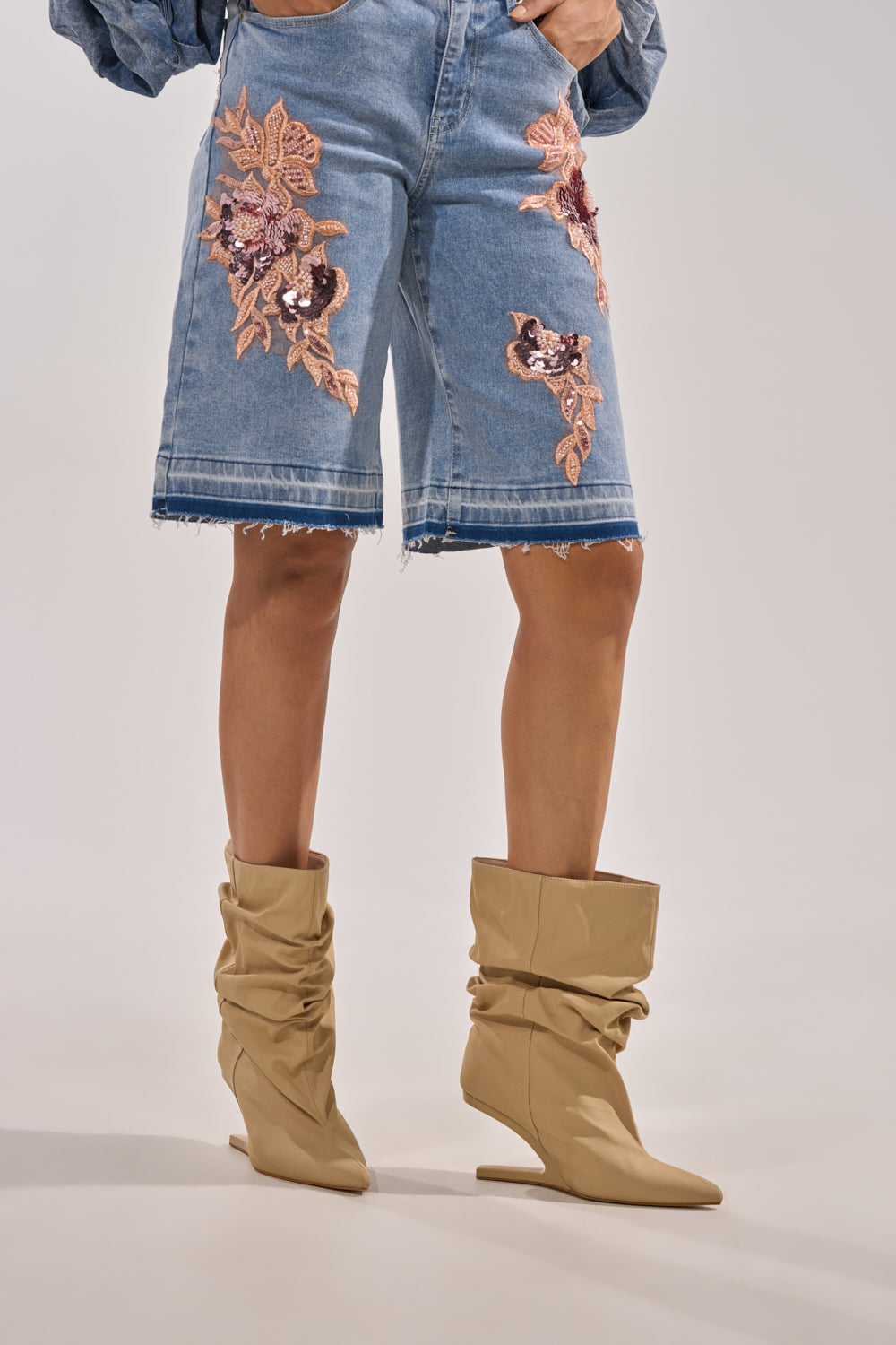 A person wearing knee-length denim shorts with pink floral embroidery and AZALEA WANG SERONA KHAKI INVISIBLE WEDGE BOOTIES stands against a plain background, with only the lower half of their body visible. 1