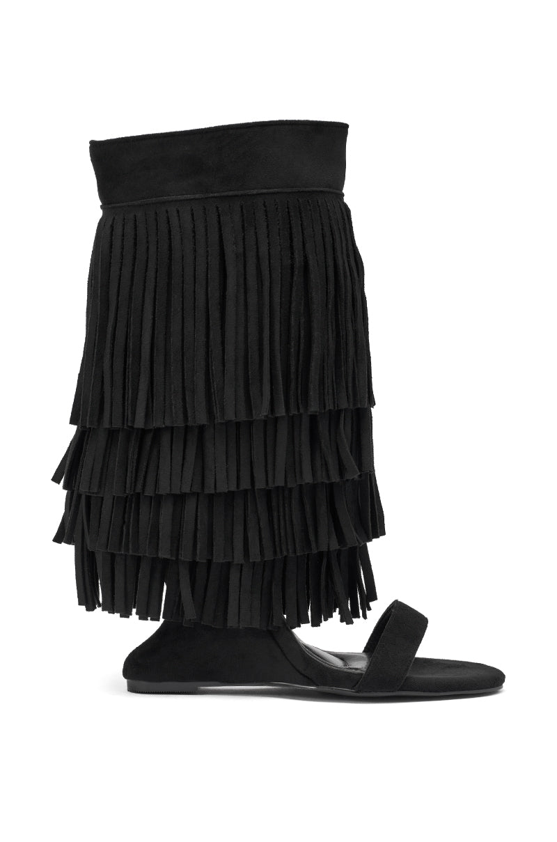 The AKIRA GOLD SESTINA Black Faux Suede Fringe Wedge Sandal features a flat, open toe, mid-calf design with long black fringe tiers for a textured, boho-chic look. 3