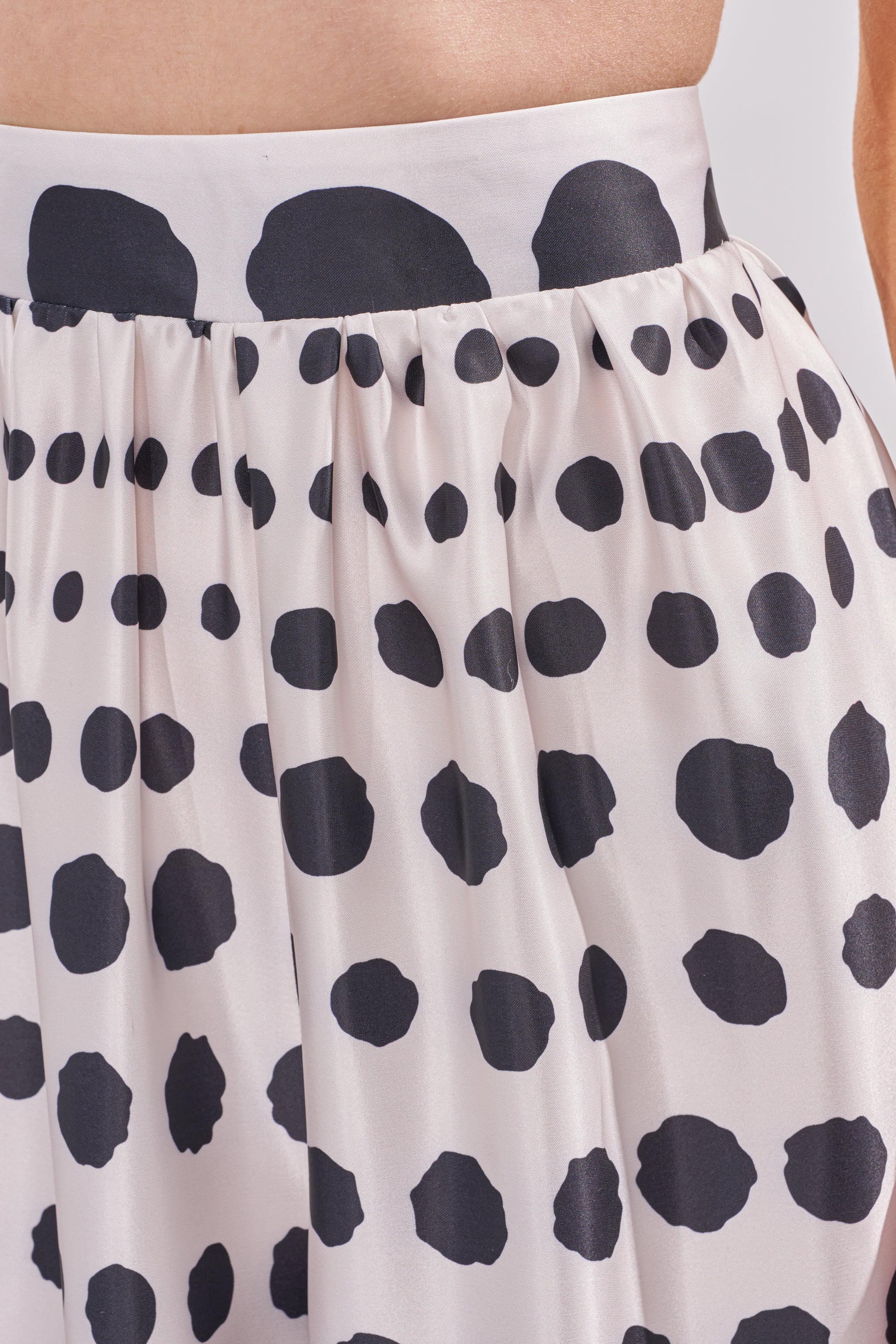 A close-up of the POLKA DOT BIKINI GIRL SET, featuring a white skirt with black irregular polka dots and a gathered waistband—ideal to pair with the matching satin bralette for your summer vacation outfit. 5