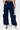 A person wearing FEEL GOOD TROUSER cargo pants in navy blue with a high-rise elastic waistband and cargo pockets, paired with a small silver handbag and pointed mesh-detailed silver heels.