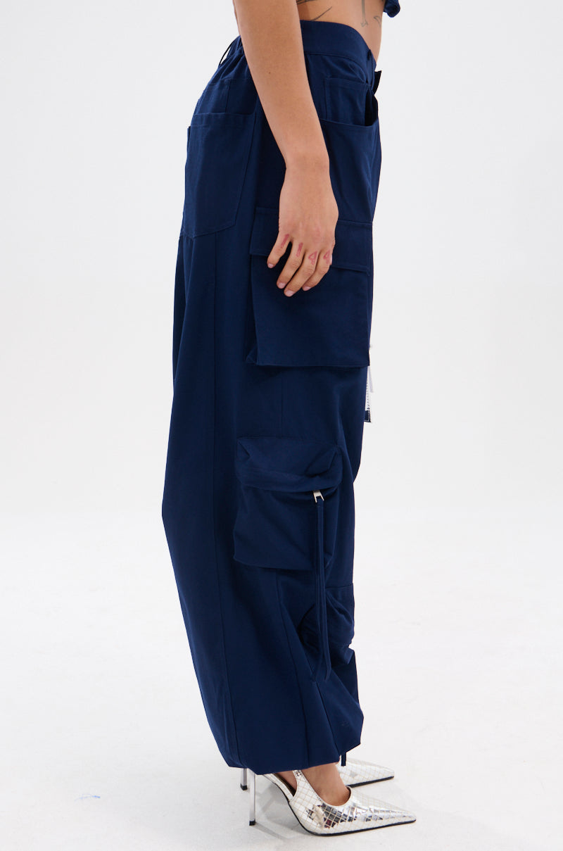 A person in profile wears FEEL GOOD TROUSER in navy with large cargo pockets and a high-rise elastic waistband, paired with silver heels, set against a plain white background.