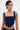 A person with short, dark, side-parted hair models the FEELING GOOD CORSET in navy blue with a square neckline. Arm and chest tattoos and facial piercings complete their look as they gaze slightly to the side.