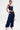 A person stands against a plain white background wearing the FEELING GOOD CORSET with a square neckline, navy cargo pants with pockets and drawstring details, silver heels, and a small silver handbag.