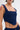A person sporting the FEELING GOOD CORSET, featuring wide straps and a square neckline. Tattoos of abstract lines and shapes are visible on their shoulder and waist. They have short hair and wear hoop earrings.