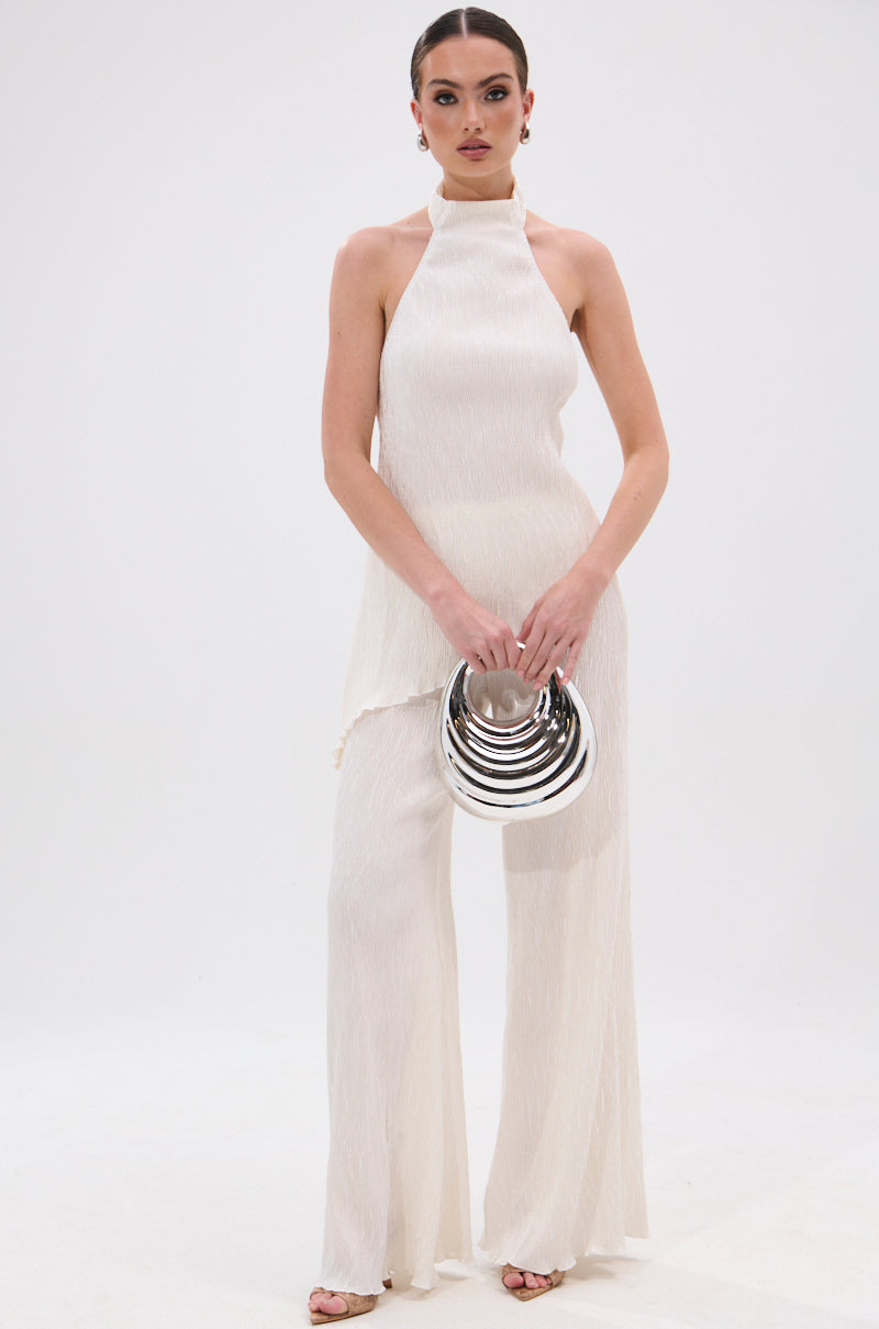 A woman stands against a white background wearing the OLIVIA PLISSE PANT IN WHITE, styled with a sleeveless top, wide-leg silhouette, metallic circular clutch, statement earrings, and her hair pulled back. 5