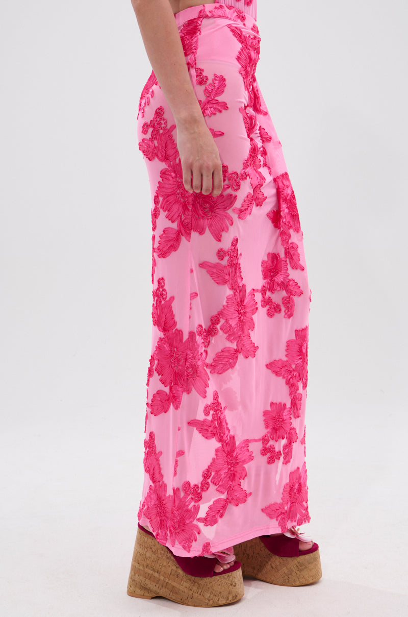 A person models the FLOWER GIRL MESH MAXI SKIRT, featuring sheer mesh with vibrant pink floral patterns, paired with platform wedge sandals. The side view shows waist to feet against a plain background.