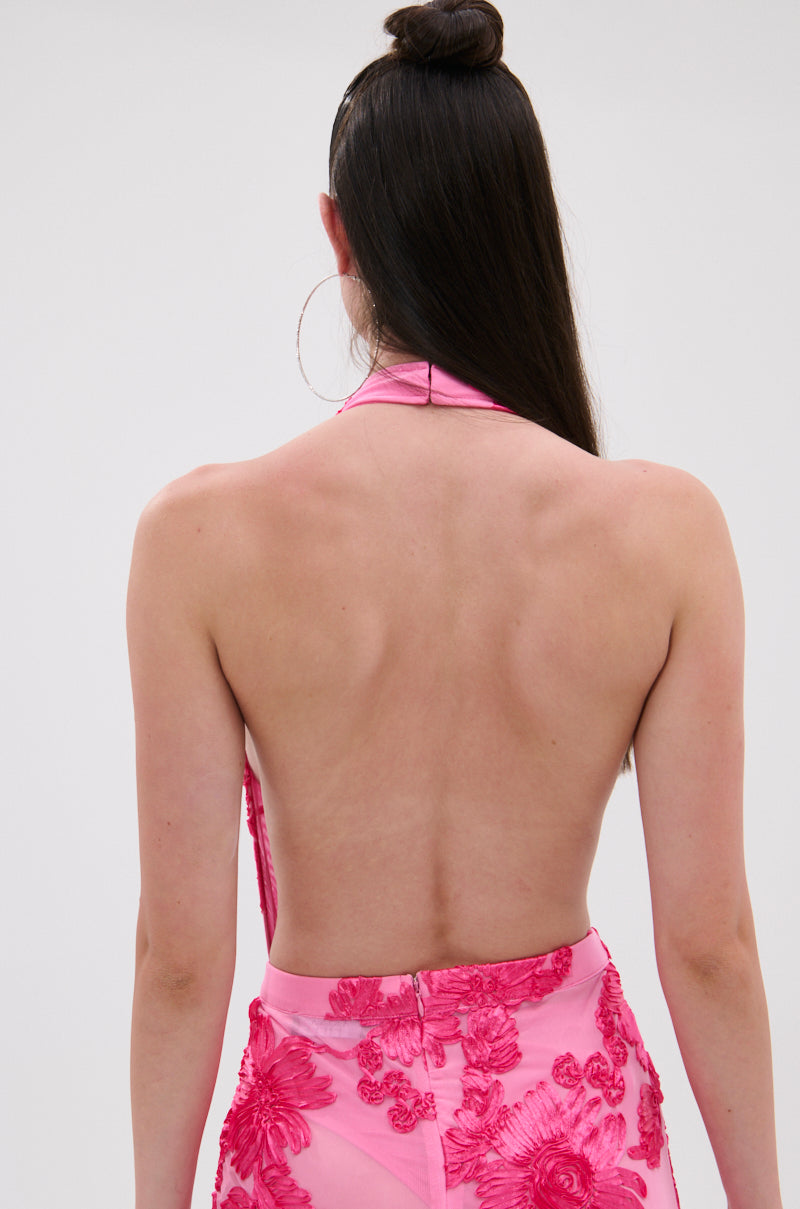 A person with long, straight brown hair is seen from behind wearing the FLOWER GIRL MESH BODYSUIT—a pink, backless piece with a halter neckline and delicate floral appliqués—set against a plain light backdrop. 3