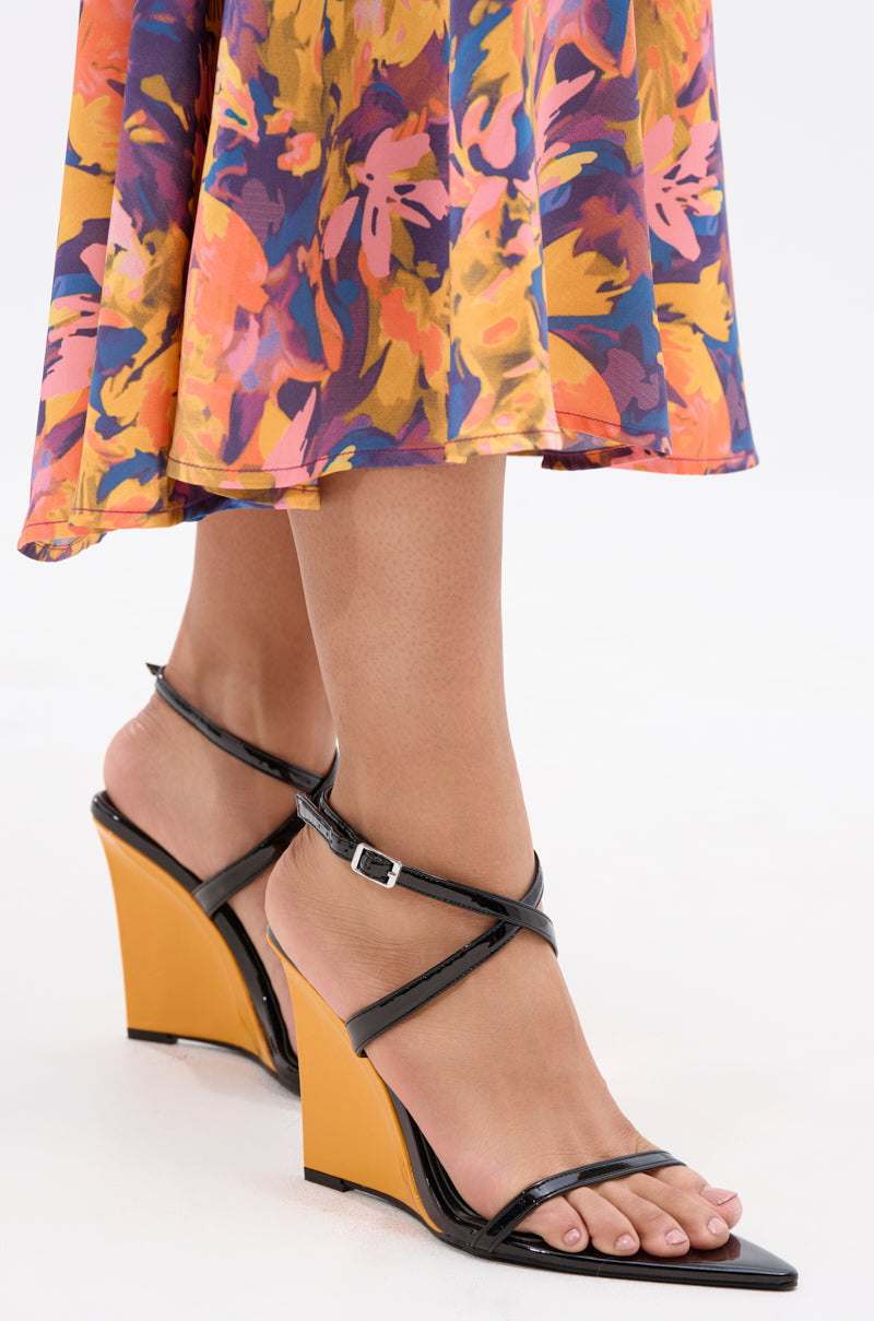 A person wearing a colorful floral skirt and AZALEA WANG SEUNG BLACK COLOR BLOCKED HEEL WEDGE SANDAL with open pointed toes and orange heels, standing on a white background.