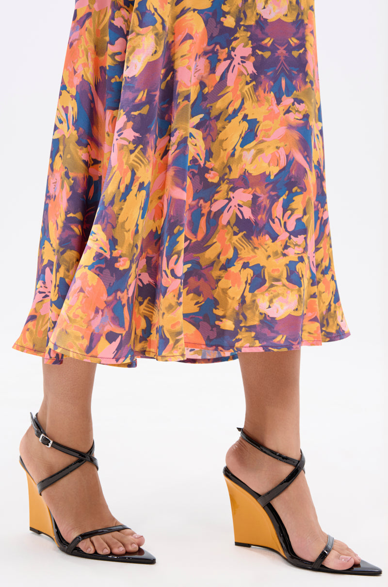 Wearing a colorful, abstract-patterned skirt, a person stands on a light background, showcasing the AZALEA WANG SEUNG BLACK COLOR BLOCKED HEEL WEDGE SANDAL with open pointed toes and mustard-yellow heels. Only the lower legs and feet are visible.