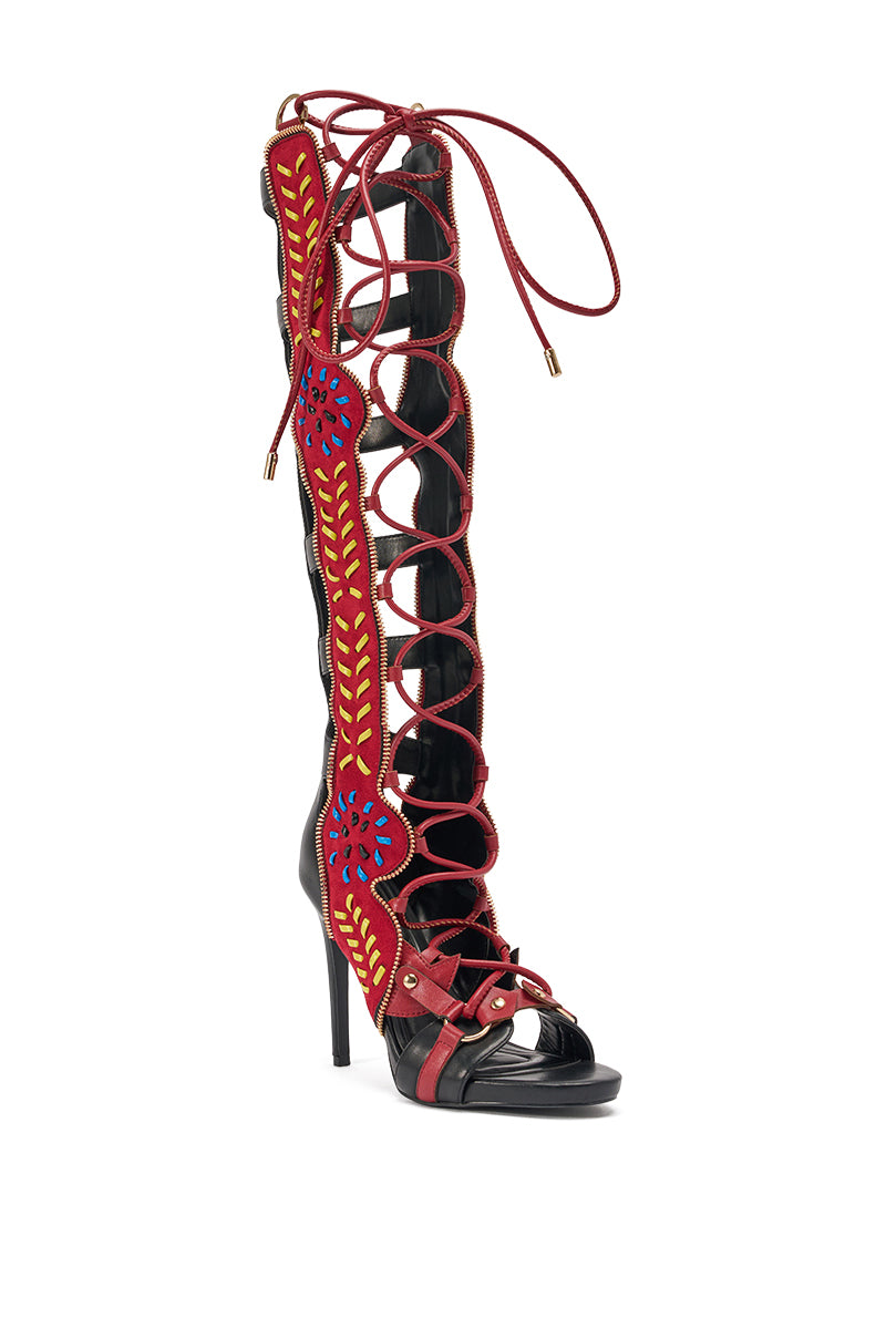 The AZALEA WANG SHAI BLACK MULTI GLADIATOR SANDAL features black stilettos with red laces, an open toe, and a bright red side panel adorned with yellow and blue embroidered floral details—a standout choice for bold style.