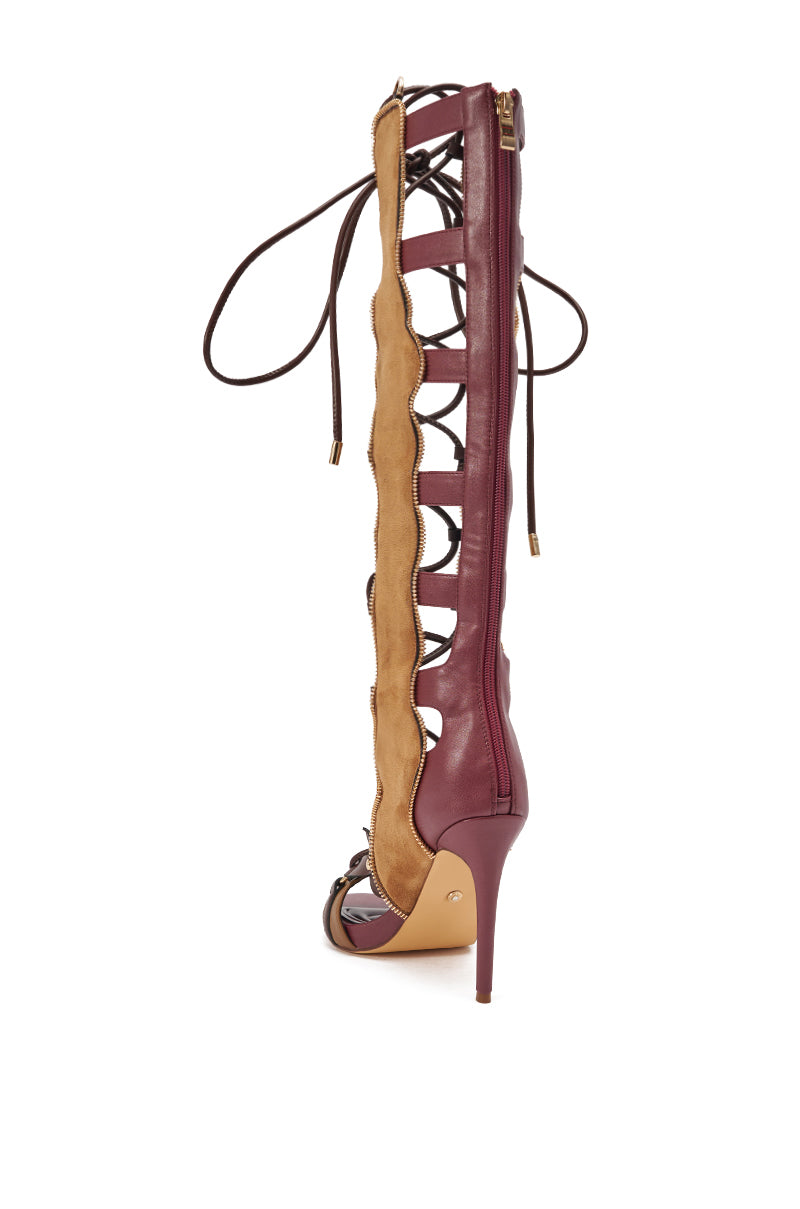 The AZALEA WANG SHAI PLUM MULTI GLADIATOR SANDAL is a tall, knee-high burgundy and tan leather sandal with a stiletto heel, open toe, and lace-up front featuring crisscross laces along the length.