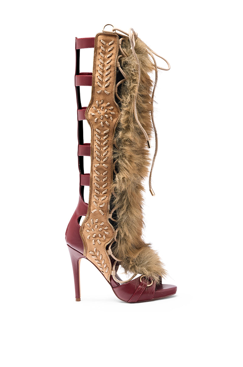 The AZALEA WANG SHAINE MULTI GLADIATOR STITCH AND FUR SANDAL is a high-heeled, open-toe sandal in maroon leather with tan stitching, side cut-outs, brown faux fur, and front laces.
