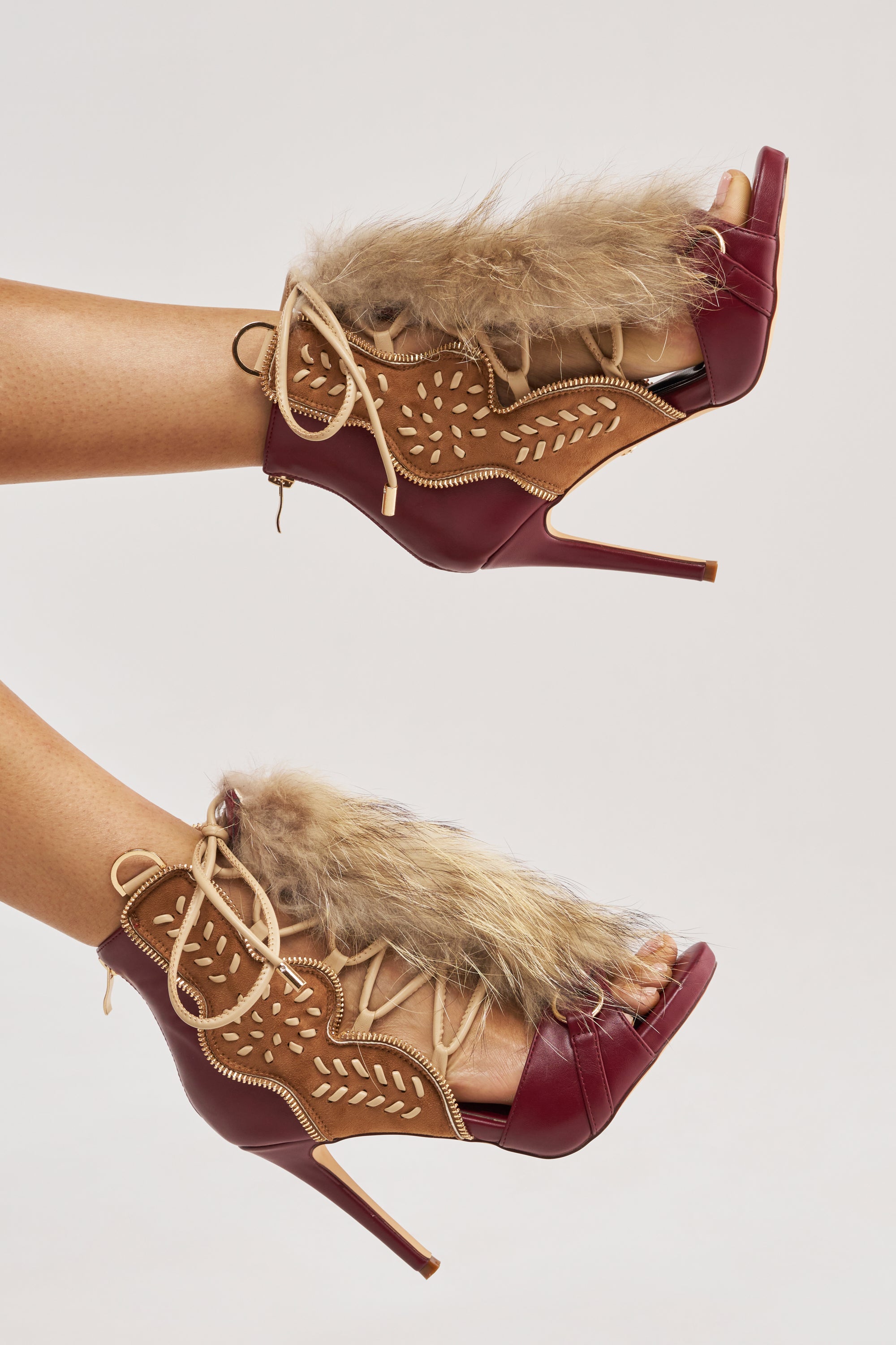 The AZALEA WANG SHAINY MULTI MATERIAL SANDAL, featuring open toes, lace-up fronts, decorative stitching, and a faux fur accent, is worn by a person with light brown skin.