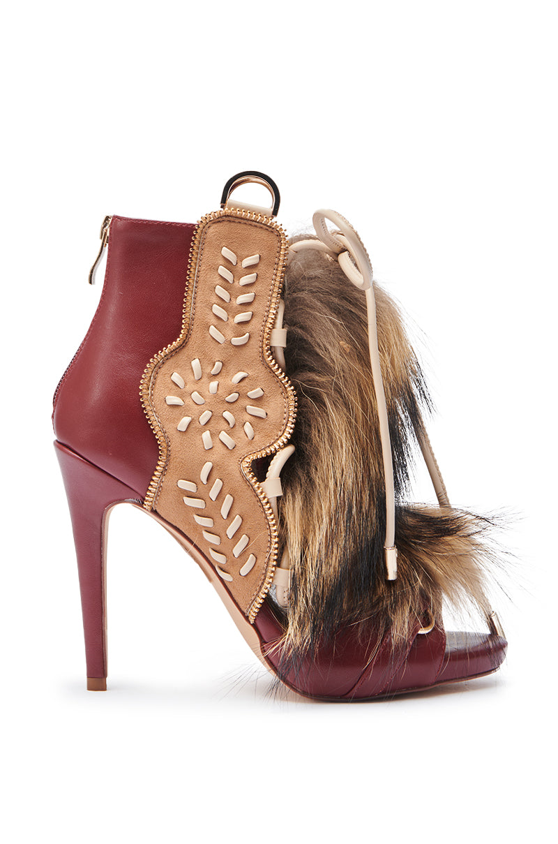 The AZALEA WANG SHAINY MULTI MATERIAL SANDAL is a high-heeled shoe with a maroon faux leather base, tan cutout details, fur accents on the front, an ankle-high shaft, back zipper, and lace-up design.