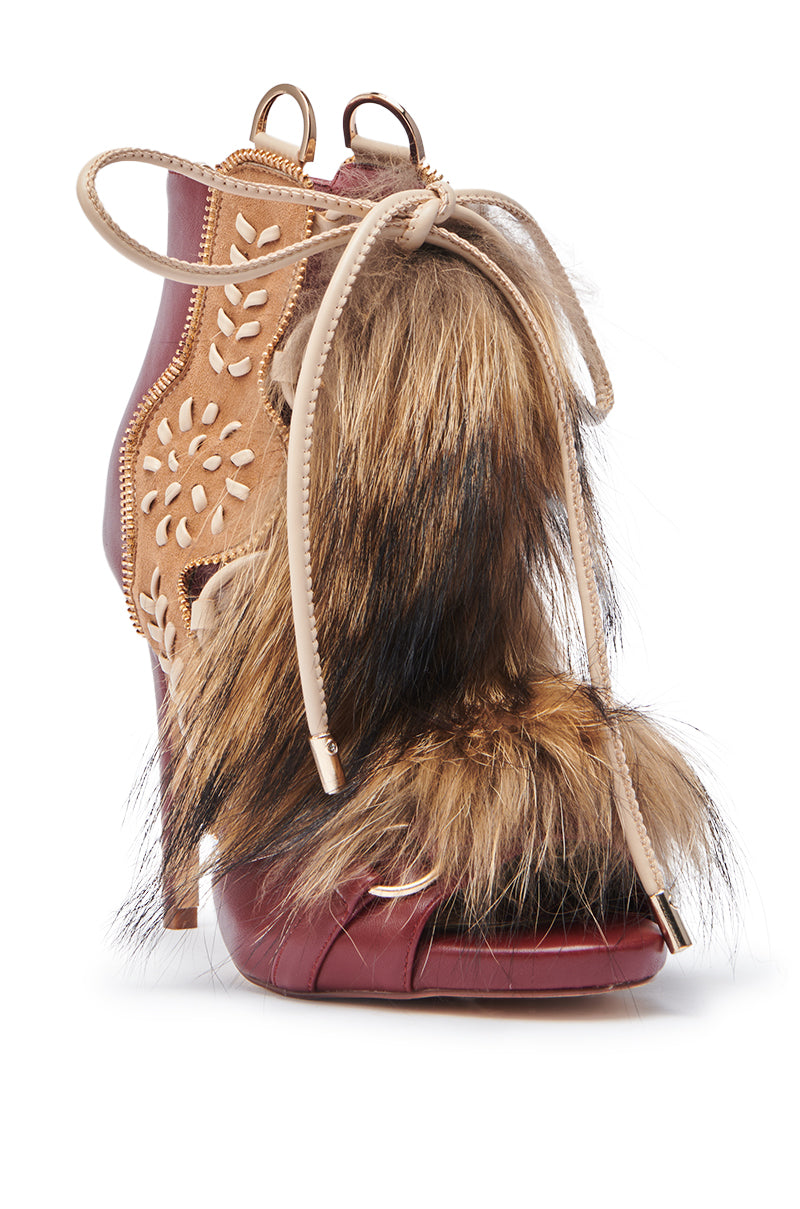 The AZALEA WANG SHAINY MULTI MATERIAL SANDAL is a high-heeled stiletto featuring burgundy faux leather, tan cutouts, beige laces, and large brown and black faux fur patches on the front and side.