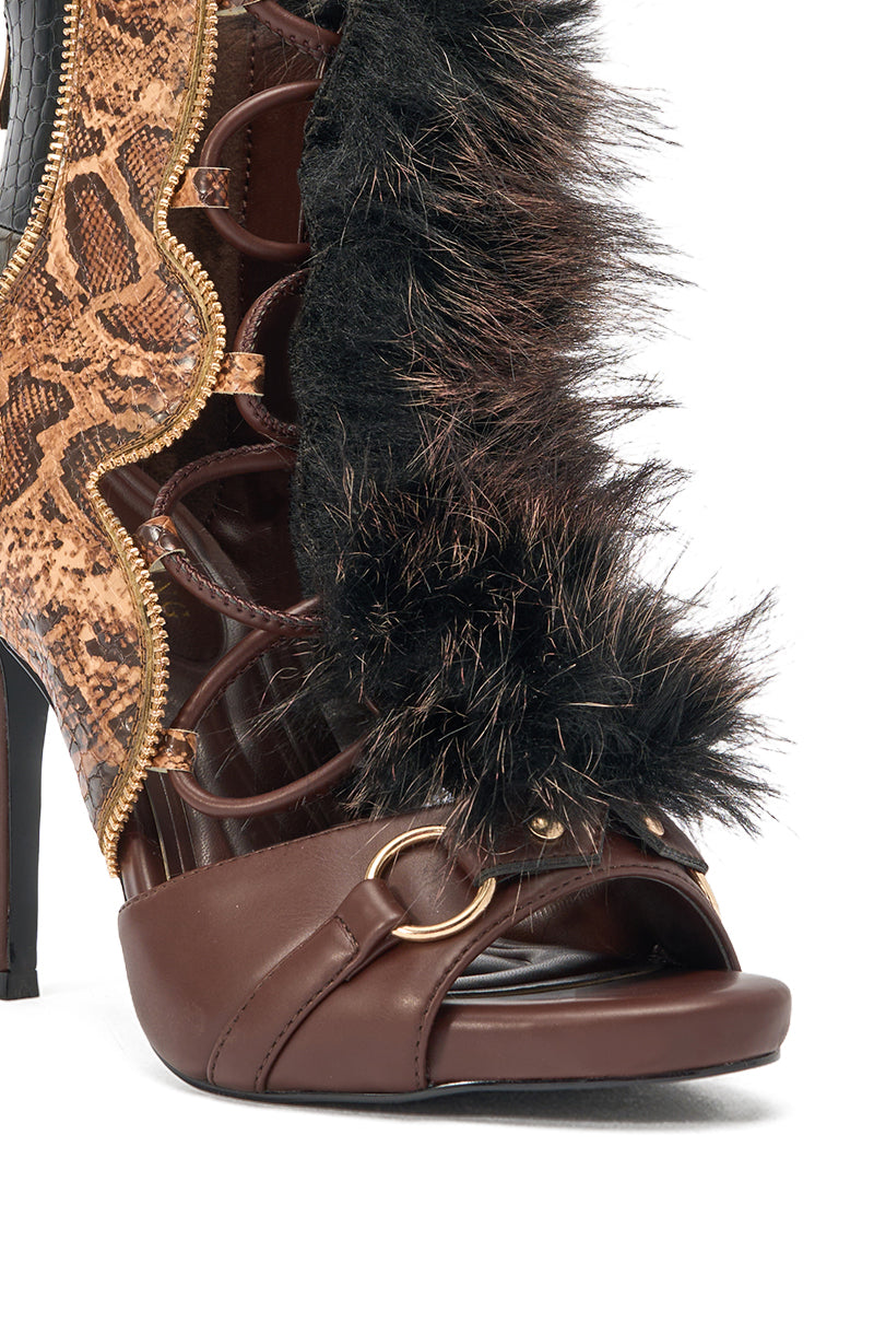 Close-up of the AZALEA WANG SHAINY SNAKE BROWN MULTI ankle heel, featuring brown leather, gold buckle, black fur trim, snake-print details, side zipper, and cutout accents against a white background. 5