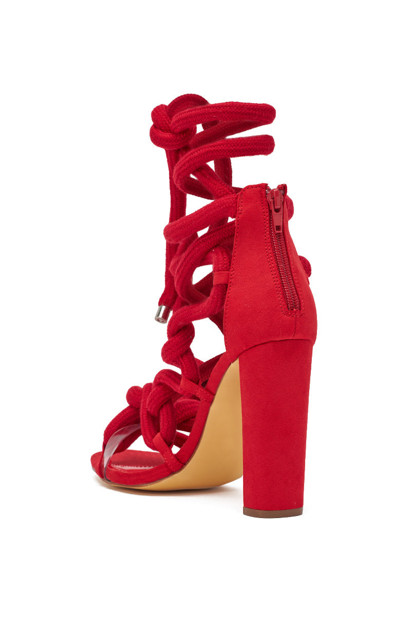 The AKIRA GOLD RED ROPE STRAP SANDAL is a red, open-toe, high-heeled sandal with chunky block heels, elaborate knotted rope lace-up straps up the ankle, and a back zipper for easy closure. 6