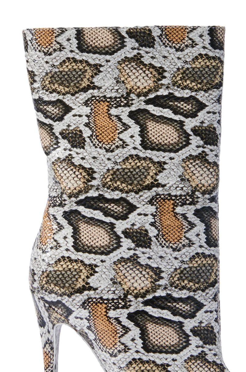 A close-up of the AZALEA WANG SIBYLLE BEIGE SNAKE COCKTAIL BOOTIE showcases its striking stiletto heel adorned with a realistic faux snakeskin pattern in shades of white, black, brown, and gray, offering a fashionable and sophisticated look.