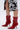 A person wearing a black and white floral skirt stands in shiny AZALEA WANG SILVA RED LACE UP STILETTO BOOTIES featuring pointed toes, thin sculptural stiletto heels, and a glossy faux patent leather finish.