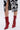 A person wearing a black-and-white floral skirt with a front slit and AZALEA WANG SILVA RED LACE UP STILETTO BOOTIE, featuring faux patent leather and sculptural heels, stands against a plain light background.