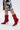A person wearing a black and white floral skirt and the AZALEA WANG SILVA RED LACE UP STILETTO BOOTIE, featuring shiny faux patent leather, pointed toes, and sculptural stiletto heels, walks on a light background.