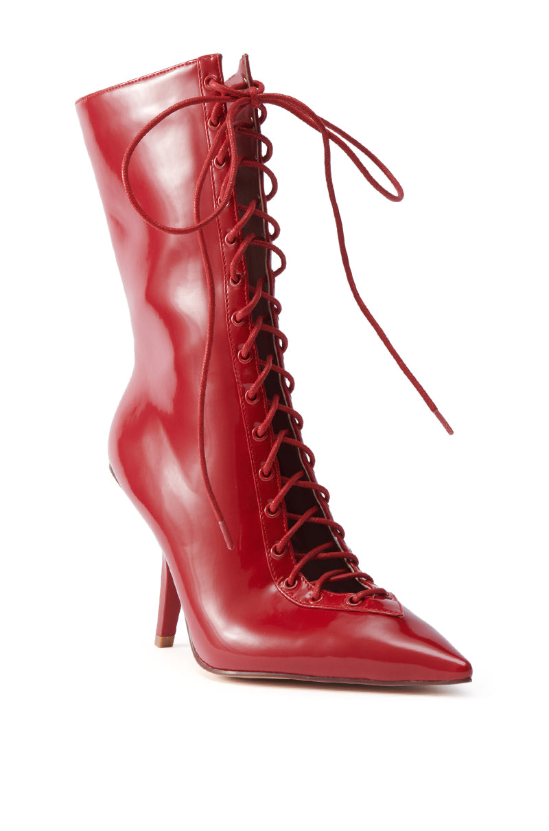 The AZALEA WANG SILVA RED LACE UP STILETTO BOOTIE features a shiny red glossy leather finish, pointed toe, sculptural high stiletto heel, lace-up front, and ankle bootie silhouette.