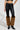 A person styled in the SIREN FUR TRIM FAUX LEATHER PANTS featuring brown faux fur accents at the ankles, paired with a black crop top and sleek black pointed boots, all set against a plain, light-colored backdrop.