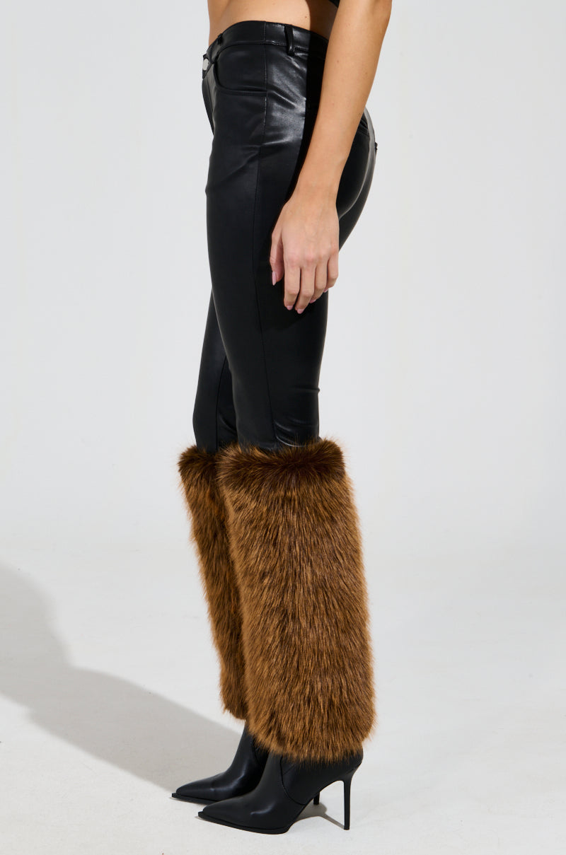 Wearing the SIREN FUR TRIM FAUX LEATHER PANTS that hug curves perfectly, complemented by chic brown faux fur leg warmers around the calves and black pointed-toe heeled boots, all set against a plain white background.