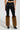 Wearing the SIREN FUR TRIM FAUX LEATHER PANTS, a person showcases a flattering silhouette in sleek black faux leather leggings. Their look is further enhanced by brown faux fur leg warmers over stylish high-heeled ankle boots as they pose with their back turned to the camera against a neutral backdrop.