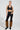 A person is dressed in black leather crop top and the SIREN FUR TRIM FAUX LEATHER PANTS, which have a curve-hugging fit. They accessorized with furry brown leg warmers, black boots, hoop earrings, and a chunky necklace against the plain white background.