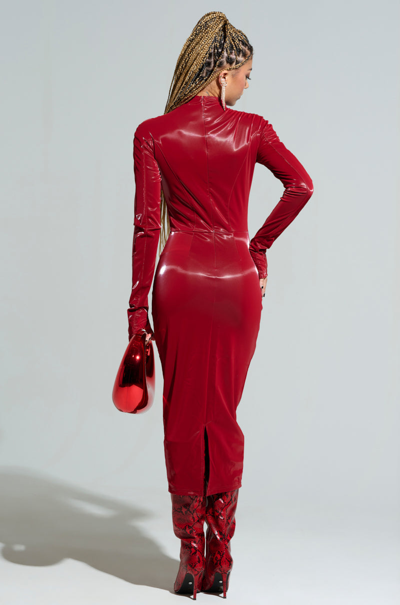 Dressed in the LIKE LIQUID FAUX LEATHER MIDI DRESS, a person with braided hair stands facing away. The vibrant red dress features a form-fitting, long-sleeve design with a high collar and a back slit. They complete their bold look with a matching red bag and knee-high red high-heeled boots.