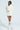 A person is posing against a plain background, dressed in a cream-colored sweater with faux fur collar and matching mini skirt. The shimmering rhinestone embellishments add subtle sparkle to the outfit. White knee-high socks and cream ankle boots finish the look as they stand with one leg crossed, showcasing their short hairstyle.