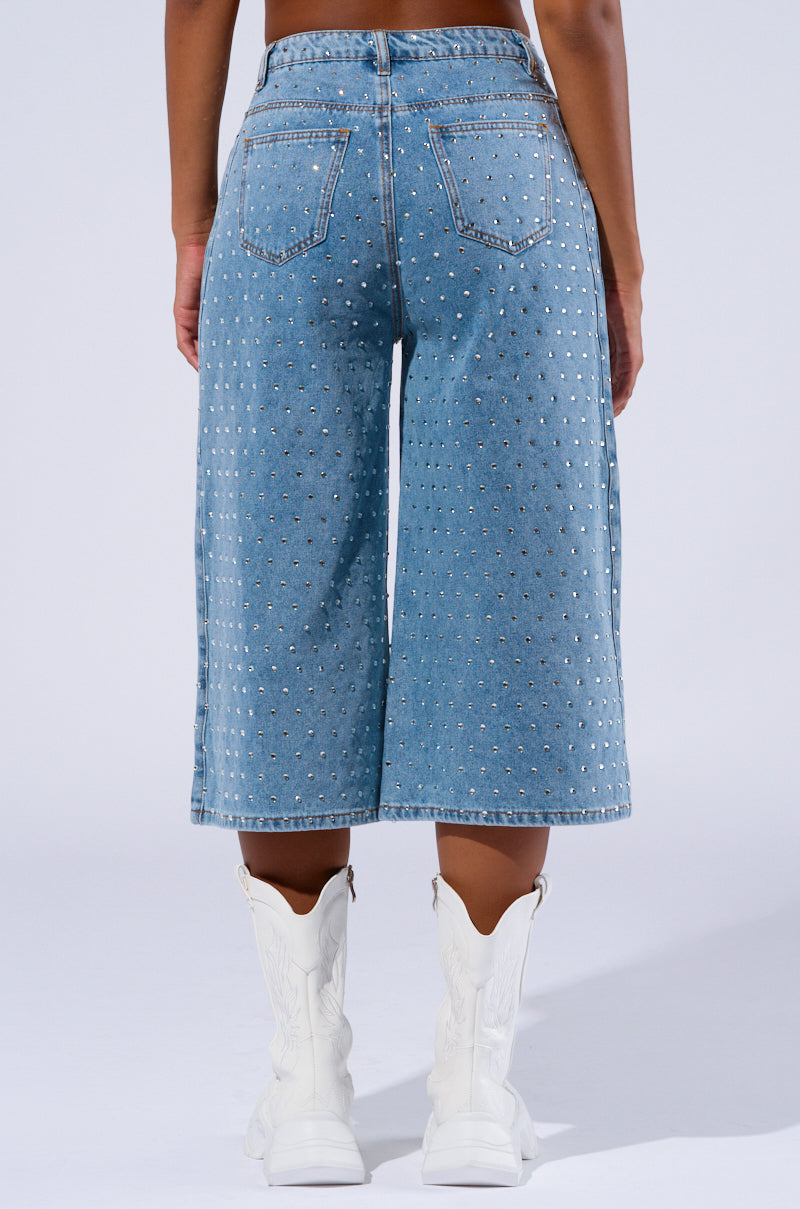 Person wearing Denim Diva Short and white cowboy boots, standing with their back facing the camera. The shorts are adorned with small rhinestone embellishments, and the boots feature embroidery and a pointed toe design.