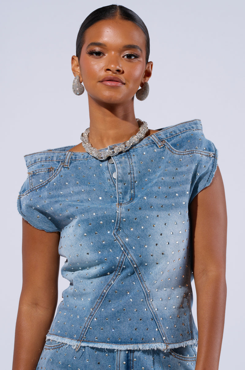 A person with smooth, dark skin and sleek, tied-back hair embodies the DENIM DIVA OFF SHOULDER TOP adorned with silver studs and AB rhinestone embellishments. They also sport a chunky silver necklace and matching earrings against a plain light gray background.