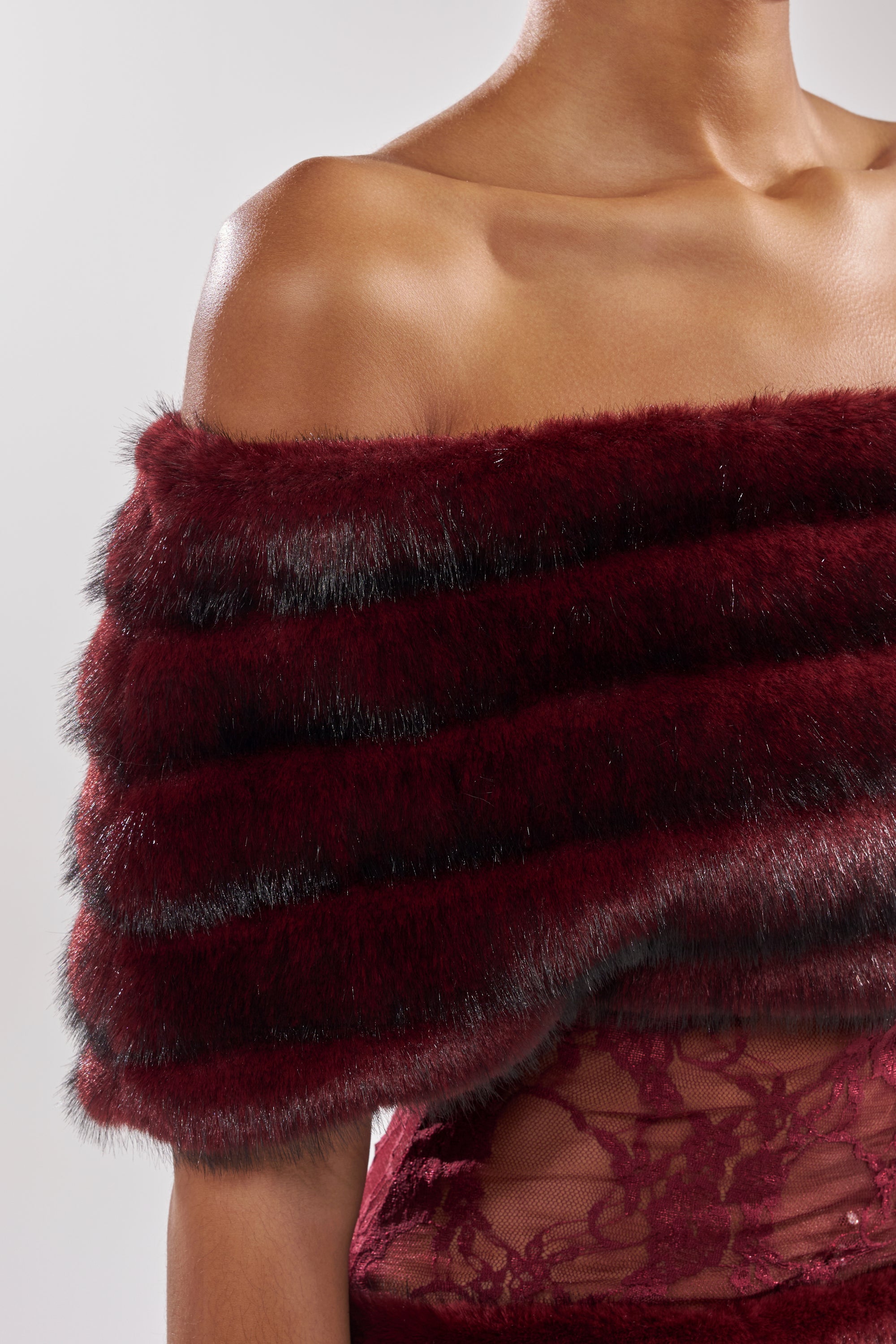 A woman showcases the SOFT CHERRY SLEEVELESS MINI DRESS, featuring sheer lace details and styled with a deep burgundy faux fur stole, seen from shoulders to waist against a neutral background.