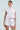 A person with vintage feminine flair stands against a light background showcasing a MIXED FLORAL PUFFER VEST. The outfit features ruffled shoulders, zip-up front, and floral patterns, completed with matching shorts adorned with pink trim.