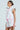 Woman in a mixed floral puffer vest with pink trim, radiating vintage feminine charm. The vest features ruffled shoulders and pairs perfectly with a skirt featuring pockets. Her sleek hair is pulled back as she stands against a light blue background, capturing timeless elegance.