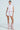 Embodying vintage feminine flair, an individual dons a white MIXED FLORAL PUFFER VEST with puffy shoulders, paired with matching shorts and pink boots, standing confidently against a plain, light backdrop.